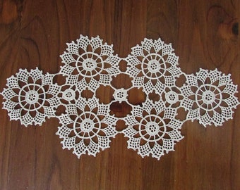 May include: White crocheted doily with a floral design. The doily is made up of five connected circles with intricate details.
