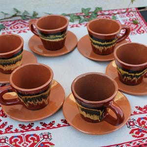 Può includere: Set di sei tazze da caffè in ceramica marrone con piattini abbinati. Ogni tazza e piattino presenta un motivo geometrico marrone, nero e giallo.