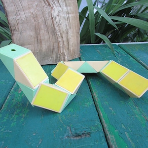 Könnte beinhalten: Ein gelbes und grünes Plastik-Puzzlespielzeug in Form einer Schlange. Das Spielzeug besteht aus mehreren dreieckigen Teilen, die miteinander verbunden und auf verschiedene Arten neu angeordnet werden können.