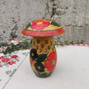 May include: A wooden mushroom-shaped container with a red, yellow, and black floral design. The container is painted with a yellow background and has a red rim.