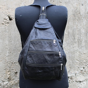 Puede incluir: Una mochila de cuero negro con varios compartimentos con cremallera. La mochila tiene una sola correa y se lleva en la espalda.