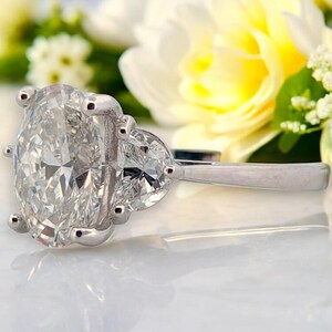 May include: A silver ring with a large oval-shaped diamond and two smaller pear-shaped diamonds on the side.