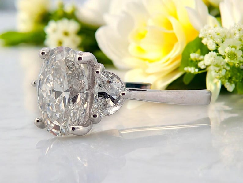 May include: A silver ring with a large oval-shaped diamond and two smaller pear-shaped diamonds on the side.