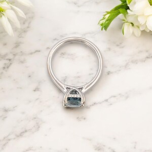 K&ouml;nnte beinhalten: Ein silberner Ring mit einem blauen Edelstein, der in einer Krappenfassung sitzt. Der Edelstein ist von einem Heiligenschein aus kleineren Diamanten umgeben.