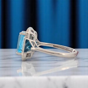 Puede incluir: Un anillo de plata con una gran gema rectangular azul claro y una piedra azul triangular m&aacute;s peque&ntilde;a. El anillo tiene un dise&ntilde;o calado detallado alrededor de las gemas.