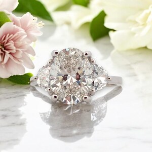 May include: A silver engagement ring with a large oval-shaped diamond surrounded by two smaller diamonds on either side.