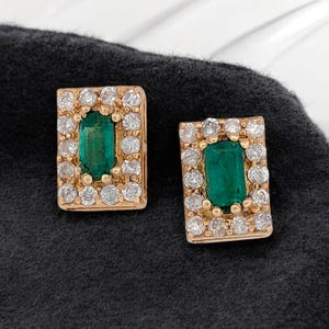 Op de afbeelding: Een paar gouden oorbellen met smaragdgroene edelstenen omringd door kleine heldere diamanten.