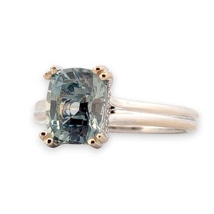 K&ouml;nnte beinhalten: Ein goldener Ring mit einem quadratischen, gr&uuml;nen Edelstein. Der Ring hat eine schlichte Band und der Edelstein ist von einer goldenen Umrandung umgeben.