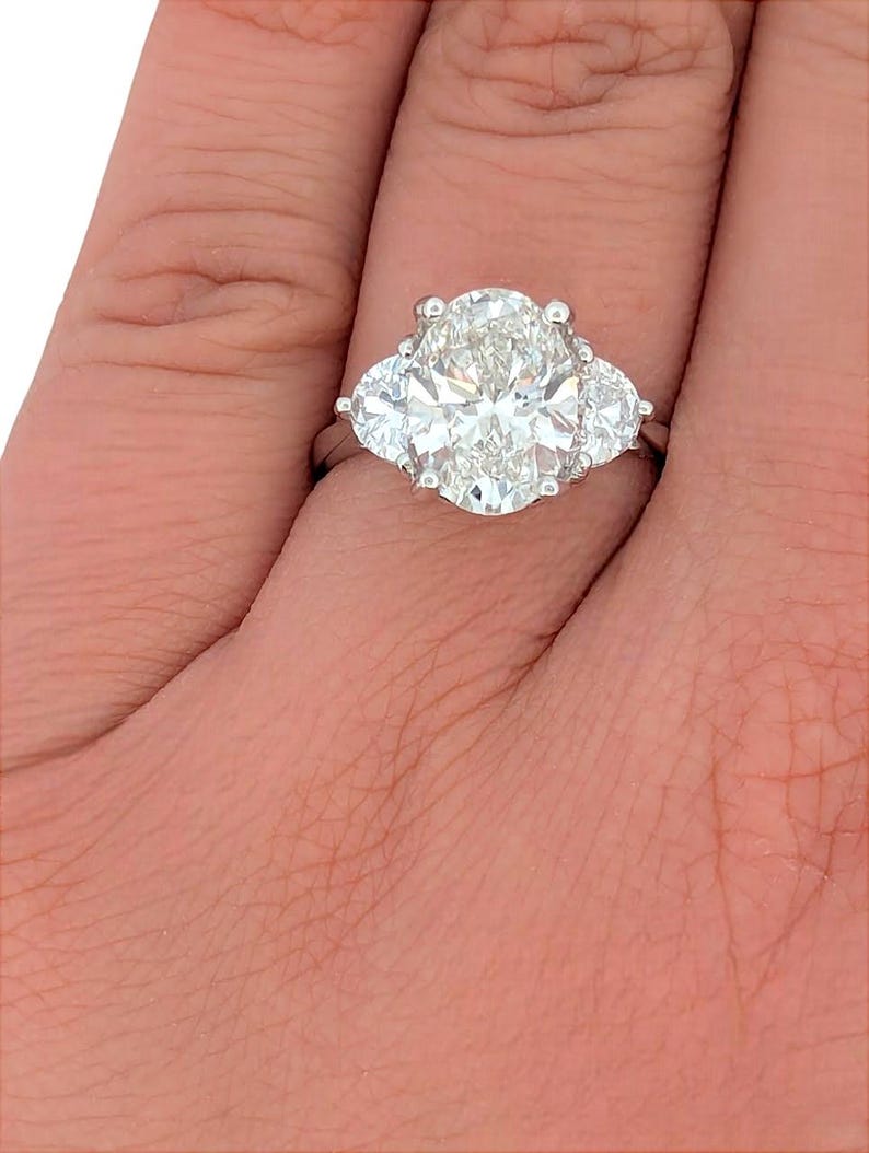 May include: A three-stone diamond engagement ring with a large oval-shaped center stone and two smaller pear-shaped stones on either side. The ring is set in platinum.