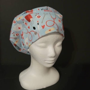 May include: A blue scrub hat with a red and white print of medical symbols and the text "proud nurse".