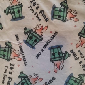 May include: White fabric with a repeating pattern of cartoon trash cans on fire. The trash cans are green with black accents and have a cute face. The text "It's fine, I'm fine" is also printed on the fabric.