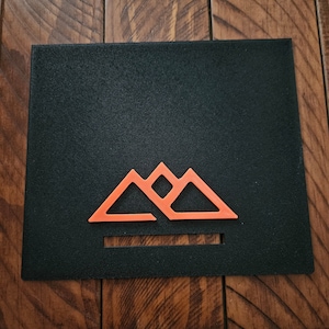 May include: A black rectangular sign with a stylized orange mountain range logo. The logo features three peaks with a horizontal line underneath.