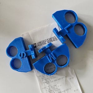 May include: Two blue plastic keychains, one shaped like the letter "S" and the other like the letter "W". Both keychains have three holes for attaching keys.