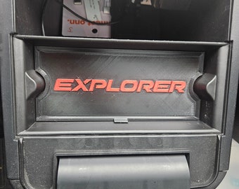 May include: A black plastic storage compartment with a red "EXPLORER" label. The compartment is open and has a small white adapter plugged into the back.
