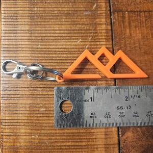 May include: Orange plastic keychain shaped like three mountains. The keychain is about 1 inch wide and is attached to a silver key ring.