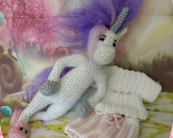 Puede incluir: Un unicornio blanco de crochet con una melena morada y rosa y un cuerno plateado. El unicornio lleva una camisa blanca de crochet y pantalones de rayas rosas y blancas.