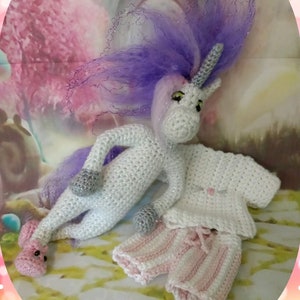 May include: A white crocheted unicorn with a purple and pink mane and a silver horn. The unicorn is wearing a white crocheted shirt and pink and white striped pants.