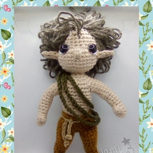 May include: A crocheted doll with brown hair, brown eyes, and a green and brown outfit. The doll is standing on a white surface. The text "Manic Yarn" is visible in the bottom right corner of the image.