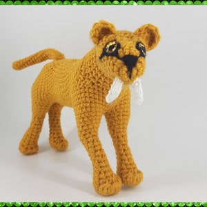 May include: A crocheted stuffed toy of a saber-toothed cat. The toy is brown with white teeth and black eyes.