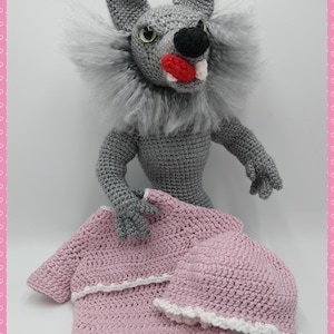 May include: A grey crocheted wolf plush toy holding a pink crocheted dress with white trim.