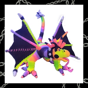 May include: A colourful crocheted dragon toy with a long, pink tongue sticking out. The dragon has a spiky mohawk, black wings, and a rainbow-coloured body.