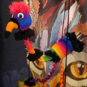 May include: A colorful crocheted flamingo puppet with a long neck and rainbow-colored legs. The puppet is hanging from strings and has a black and white patterned body.