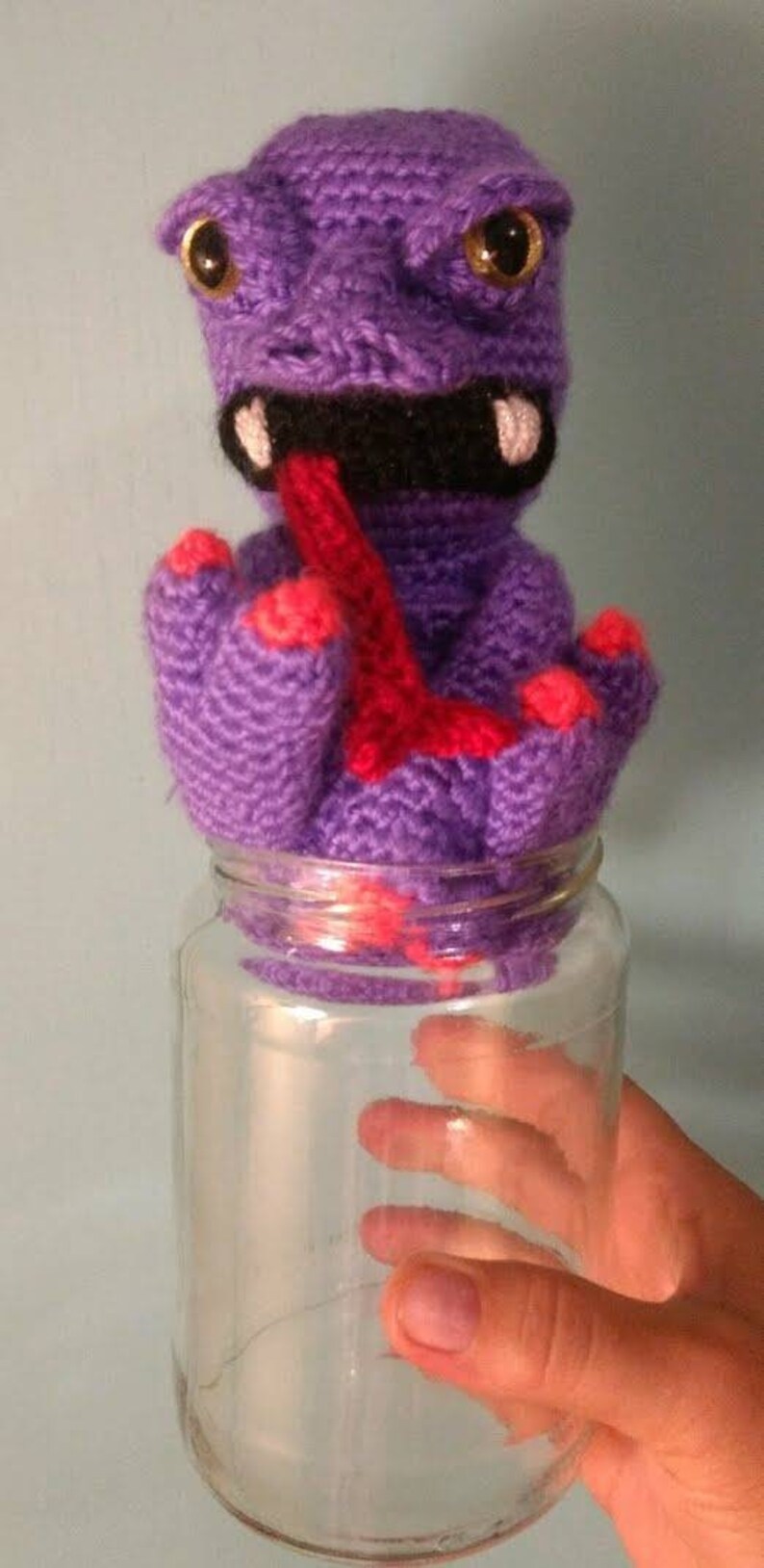 May include: Purple crocheted monster with a red tongue sticking out, sitting inside a clear glass jar.