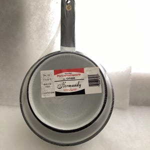 May include: A grey porcelainware sauce pan with a long handle, featuring a speckled finish and a black rim. A rectangular label on the base reads Gourmet Porcelainware by Cinsa Normandy, No. 161, 1 2 QT, SAUCE PAN, 1116707/BM, and Made in Mexico.