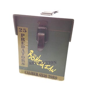May include: A green wooden box with a metal clasp and hinge. The box has the text "25 PREDATORS" on the side, along with "The Bohemian Revolution" and "Caliber 6X50 Toro" in yellow.