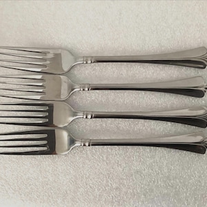 May include: Four silver forks with ornate handles. The forks are arranged in a row, with the handles pointing to the right.