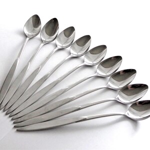 May include: A collection of eight polished silver spoons arranged in a fan shape. Each spoon has a slender, elongated handle and a rounded bowl. The spoons are displayed against a white background, highlighting their reflective surfaces.