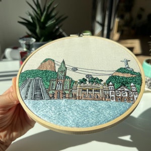 Puede incluir: Arte de bordado en aro que representa una ciudad de R&iacute;o de Janeiro, Brasil. La escena incluye la ic&oacute;nica estatua del Cristo Redentor, el Pan de Az&uacute;car y un telef&eacute;rico.