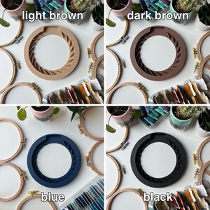 May include: Four embroidery hoops with different colored silicone inserts. The colors are light brown, dark brown, blue, and black. The hoops are on a white surface with other craft supplies.