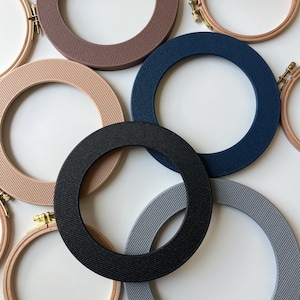 May include: Assortment of embroidery hoops in various colors, including beige, dark blue, gray, and black. The hoops are made of plastic and have a ribbed texture.