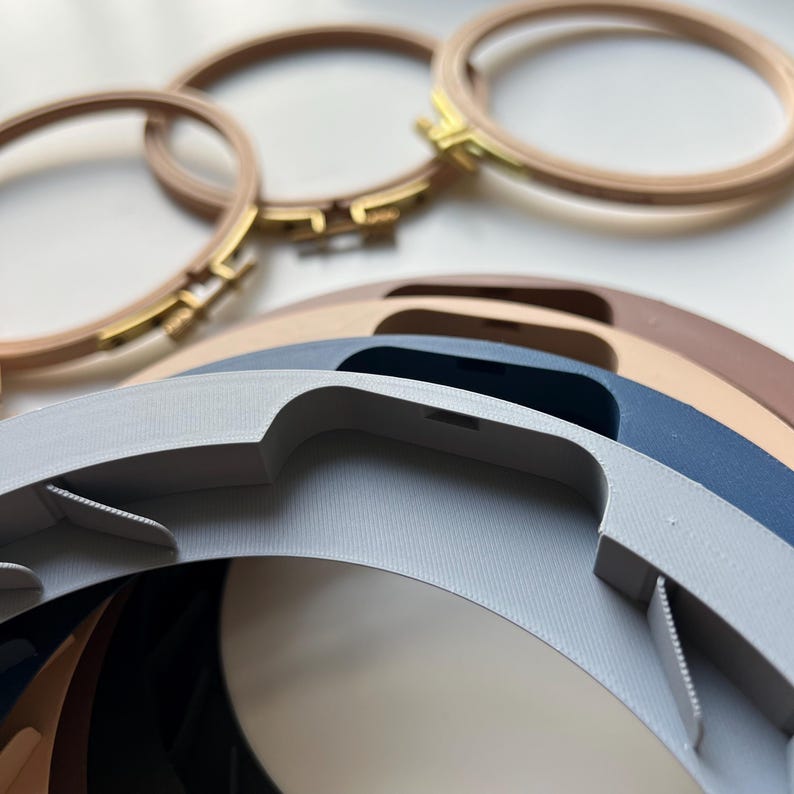 May include: A set of four embroidery hoops in various sizes. The hoops are made of wood and have a natural finish. The hoops are stacked on top of each other, with the largest hoop at the bottom and the smallest hoop at the top.