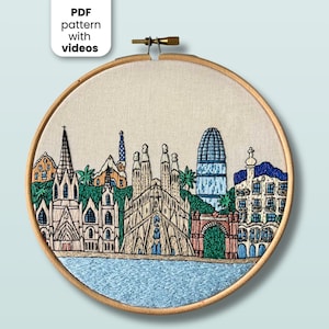 May include: A circular wooden embroidery hoop containing a hand-stitched fabric panel depicting a city skyline. The design features architectural landmarks in shades of beige, blue, and green, with the text PDF pattern with videos visible.