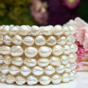 May include: A multi-strand bracelet composed of numerous white, irregularly shaped baroque pearls. The pearls exhibit a lustrous, iridescent surface and are strung together in a dense, layered formation, creating a textured, rounded appearance.
