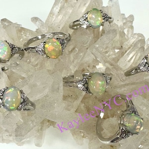 May include: Six silver rings with opal gemstones. Each ring features a delicate floral design with a central oval-shaped opal. The opals are iridescent with shades of white, yellow, and green.