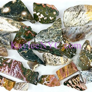 May include: A collection of 20+ natural green, brown, white, and pink ocean jasper rough stones. The stones are various shapes and sizes.