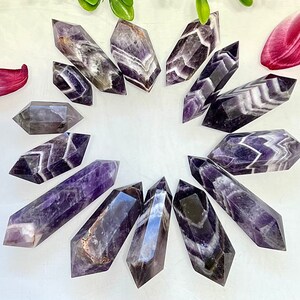 May include: A collection of 14 amethyst points with a variety of purple and white banding patterns. The points are arranged in a circle on a white background.