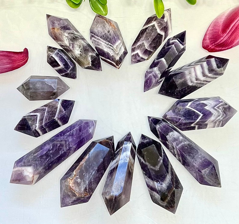May include: A collection of 14 amethyst points with a variety of purple and white banding patterns. The points are arranged in a circle on a white background.