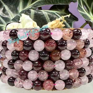 May include: A strand of pink and burgundy gemstone beads. The beads are round and have a translucent appearance. The beads are arranged in a circular pattern.