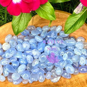 May include: A collection of blue lace agate tumbled stones in a wooden bowl. The stones are smooth and polished, with a light blue color and white banding.