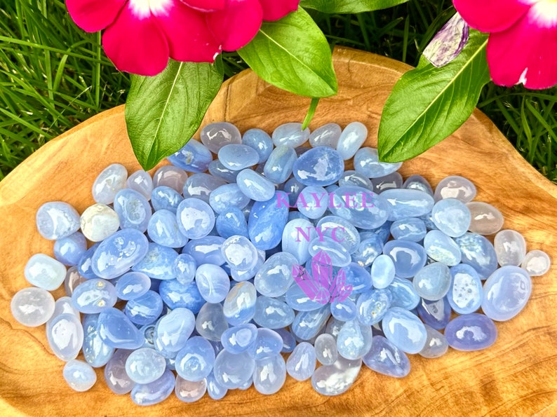May include: A collection of blue lace agate tumbled stones in a wooden bowl. The stones are smooth and polished, with a light blue color and white banding.