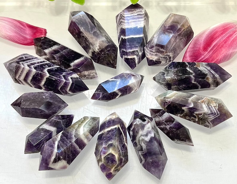 May include: A collection of 12 amethyst chevron points, each with a unique pattern of purple and white stripes. The points are arranged in a circle on a white surface.