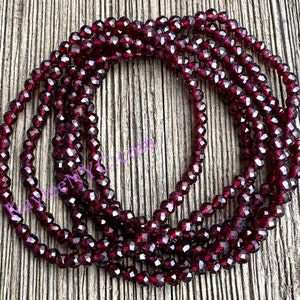 May include: A strand of deep red faceted glass beads. The beads are small and round, and they are strung together on a clear thread. The beads are arranged in a circle, and they are lying on a wooden surface.