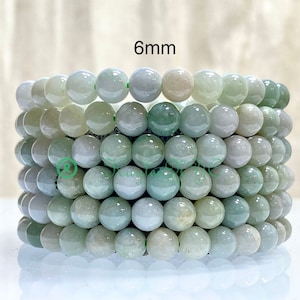 May include: Six bracelets of 6mm jade beads in varying shades of green and white. The beads are strung together, creating a stack of bracelets. The text "6mm" is visible in the upper right corner.