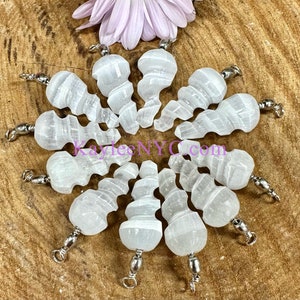 May include: Ten white selenite crystal pendants with silver jump rings. The selenite crystals are carved in a spiral shape.