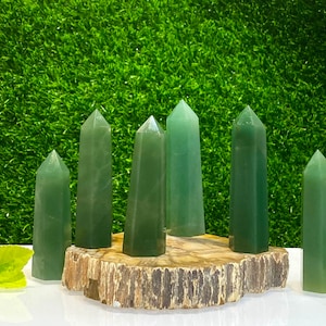 Puede incluir: Siete puntas de cristal verde dispuestas sobre una rodaja de madera. Las puntas son de varios tonos de verde y tienen un acabado liso y pulido.