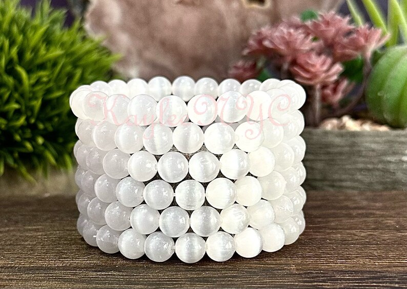 Puede incluir: Una pila de cuentas de cristal de selenita blanca, cada cuenta es lisa y redonda. Las cuentas est&aacute;n dispuestas en un patr&oacute;n circular, creando un brazalete o un collar.